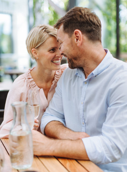 Portrait of beautiful couple in a restaurant, on a romantic date. Wife and husband touching foreheads, having romantic moment at restaurant patio.